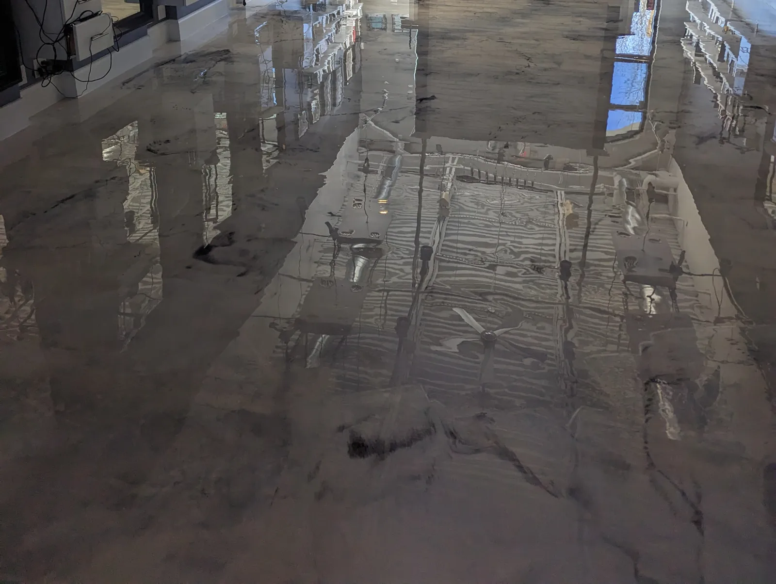 Close view of a glossy marbled gray and white floor reflecting shelving, windows and ceiling fixtures in a retail interior.