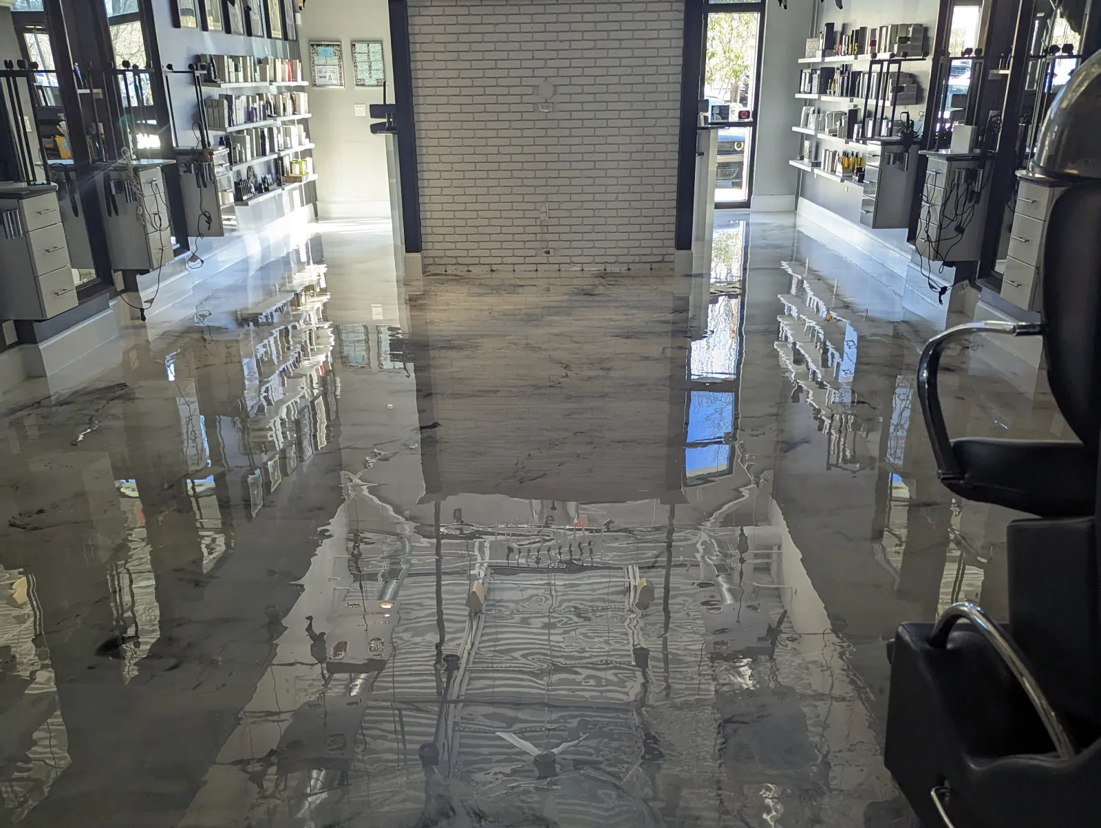 A glossy marbled gray and white metallic floor in a retail interior, reflecting wall shelving, a white brick feature wall and styling stations.
