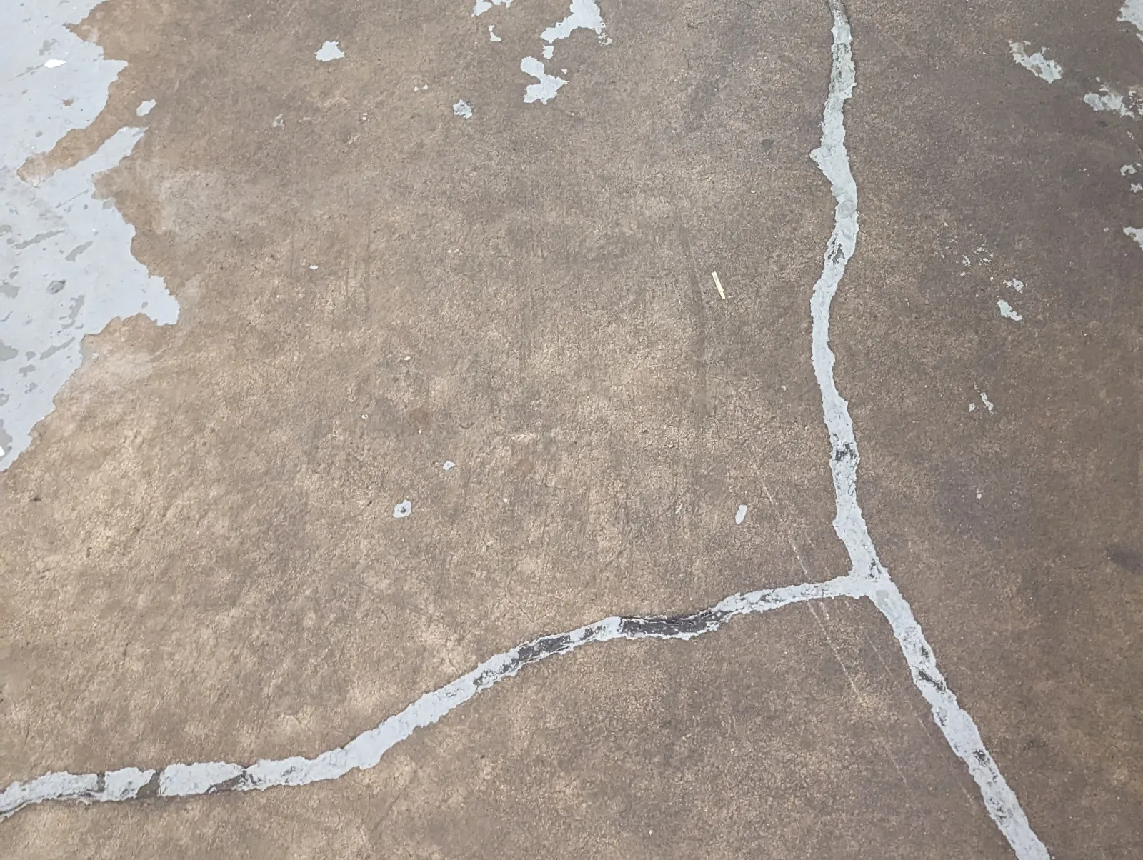 Bare brown concrete where an older gray coating has worn away in patches, with light gray lines following cracks across the slab.