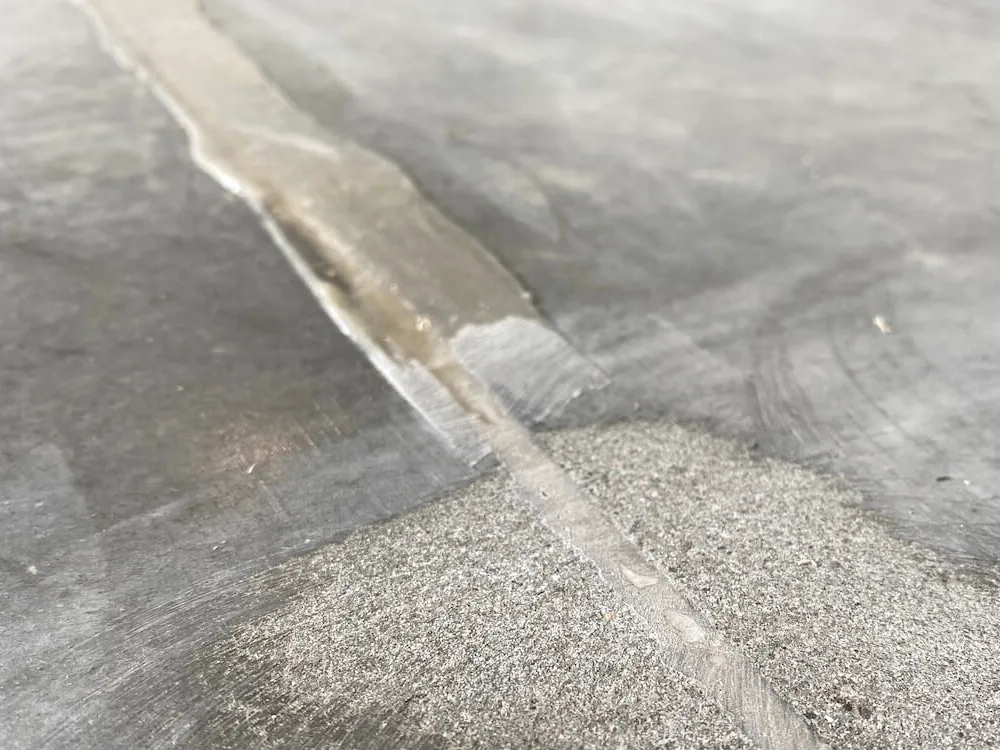 Close view of a joint in a concrete slab filled with a pale material and tooled roughly level, with circular grinder marks visible in the concrete on either side.