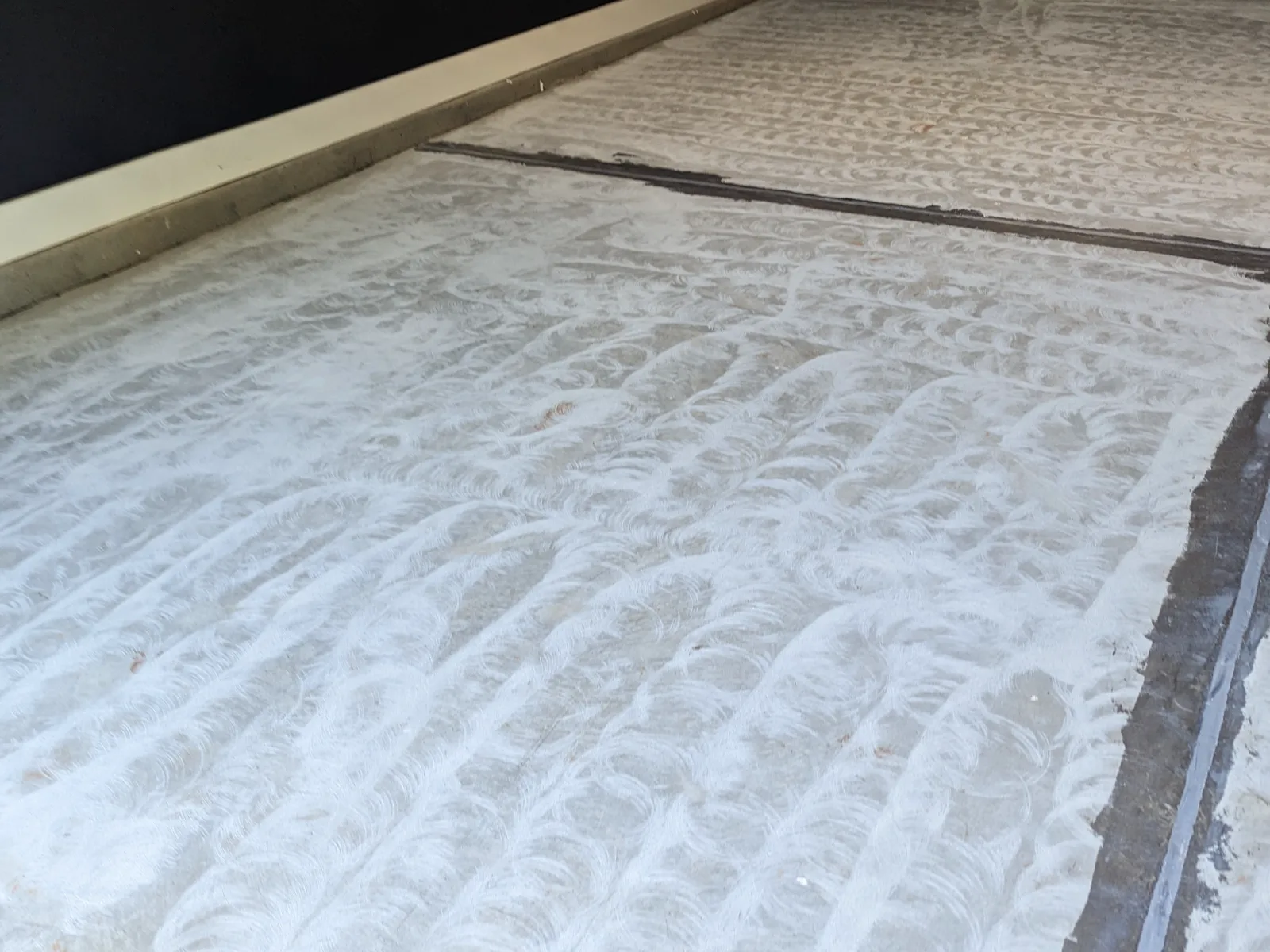 A concrete slab after grinding, showing overlapping circular marks across the whole floor and two filled joint lines running through it.