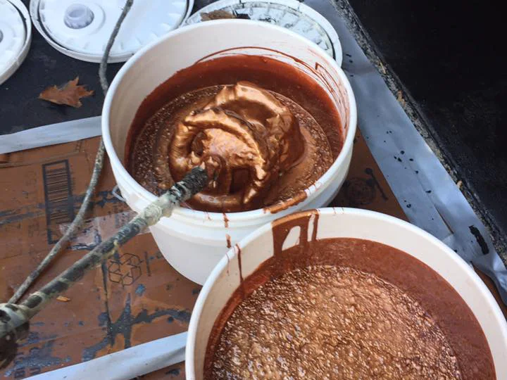 Two mixing buckets on a work sheet, one holding copper-toned metallic pigment part-way through being blended into resin with a paddle, the other already mixed.